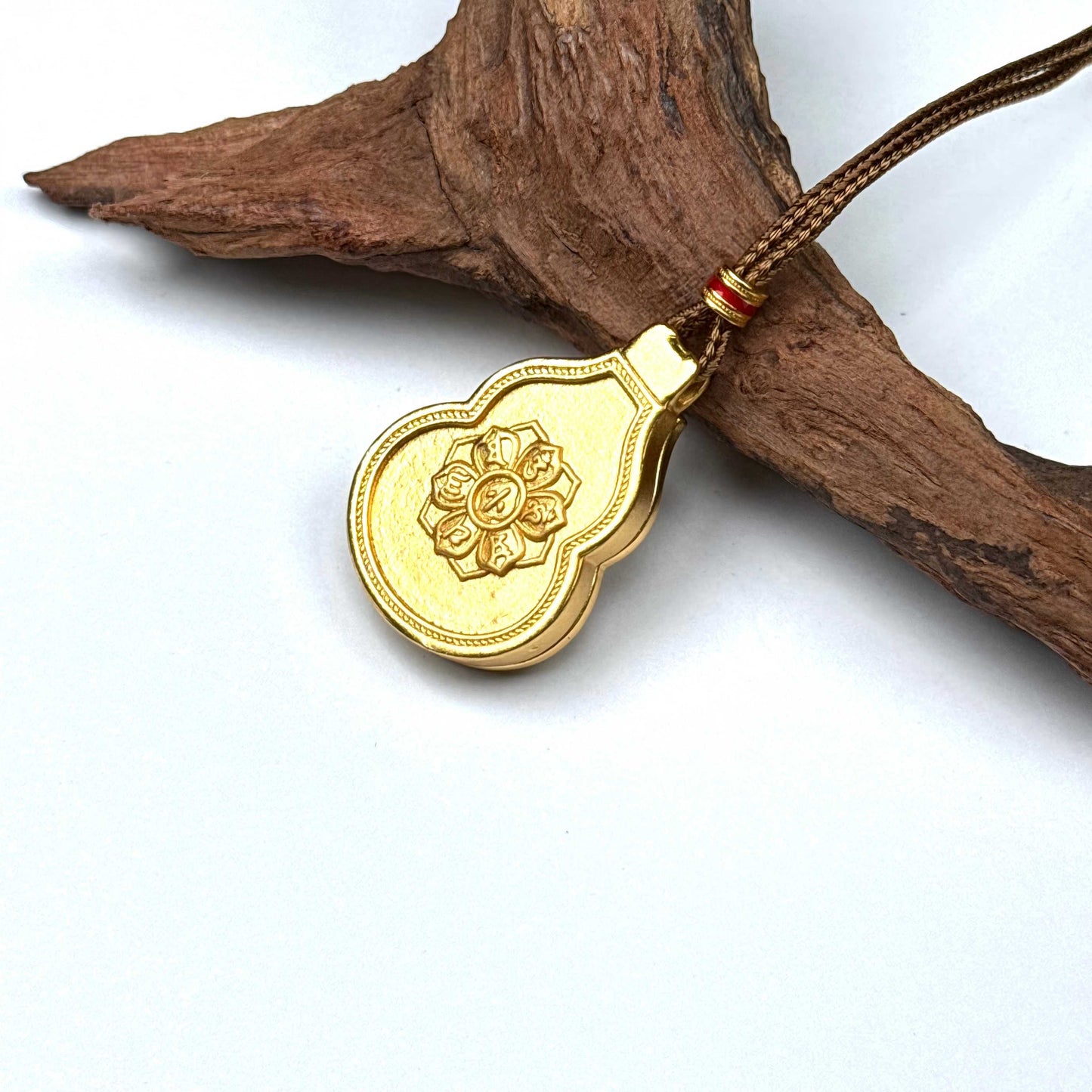 The embossed lotus mandala back side of a sand gold gourd charm necklace resting against natural rustic wood.