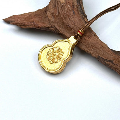 The embossed lotus mandala back side of a sand gold gourd charm necklace resting against natural rustic wood.