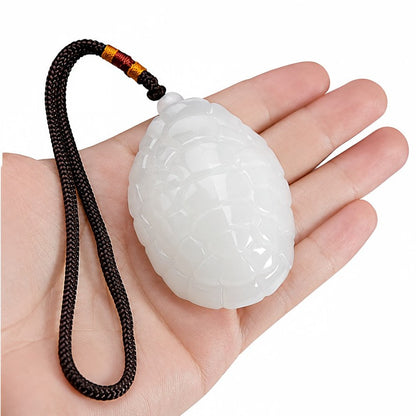 White jade turtle amulet held in an open palm, showing the carved shell front and braided cord
