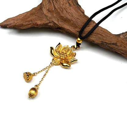 A beautiful traditional sand gold filigree lotus amulet resting elegantly on a piece of rustic driftwood, highlighting its Zen Buddhist design.