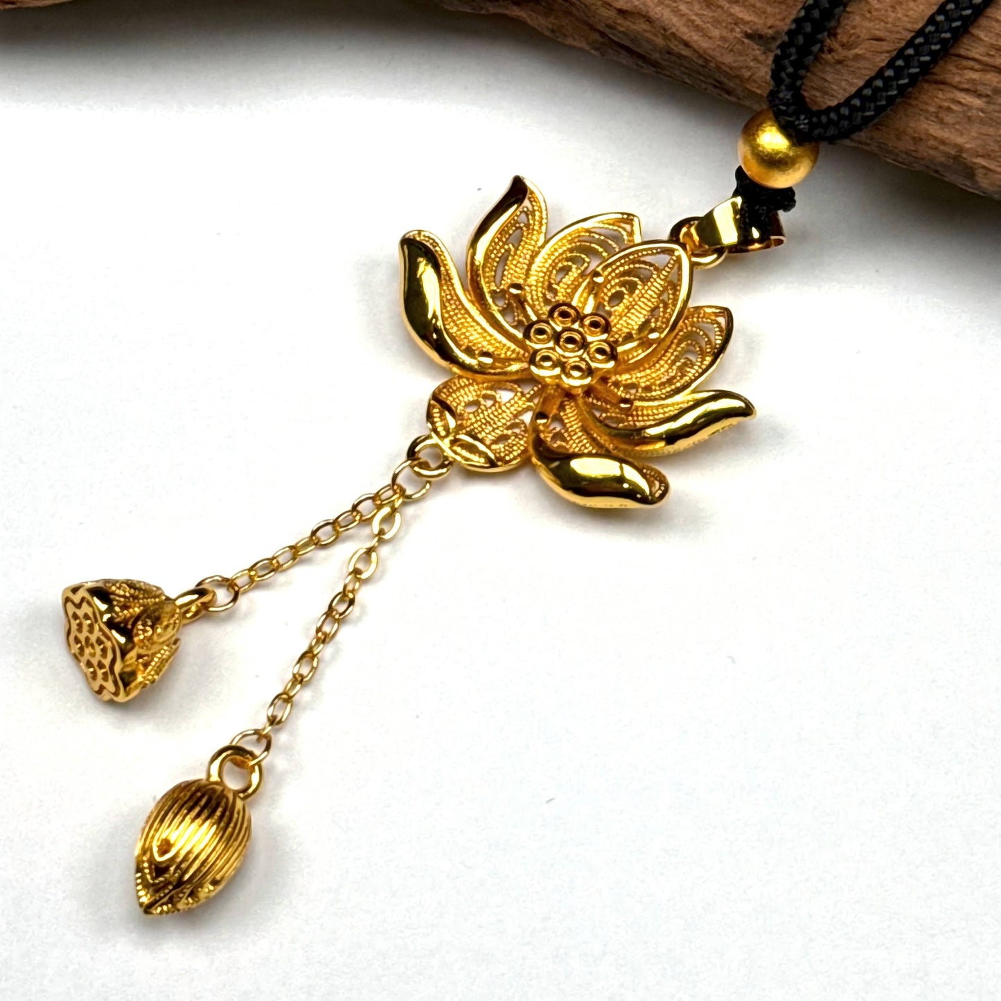 A beautiful traditional sand gold filigree lotus amulet resting elegantly on a piece of rustic driftwood, highlighting its Zen Buddhist design.