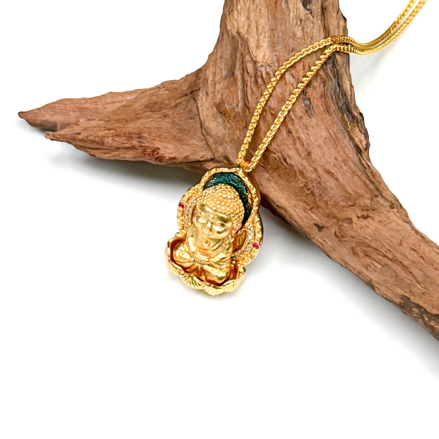 Close-up angled view of a golden Buddha pendant resting on natural driftwood, showcasing the detailed lotus throne and rich 24K gold hue.