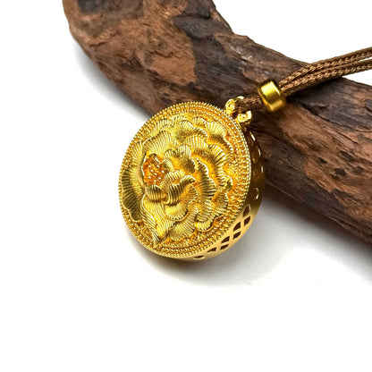 Angled view of a sand gold filigree blessing charm on natural wood, displaying the carved plaque for prosperity and delicate openwork craftsmanship.