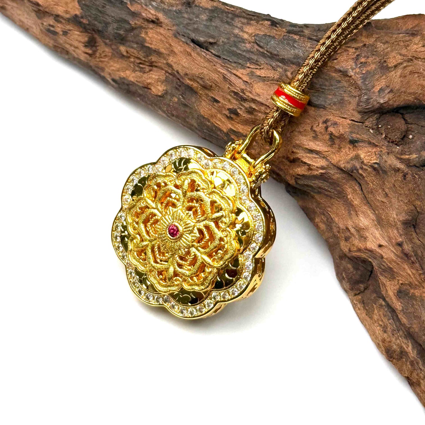 A luxurious sand gold fortune wheel pendant with shimmering red gemstones resting elegantly on rustic driftwood for a high-end Zen aesthetic.