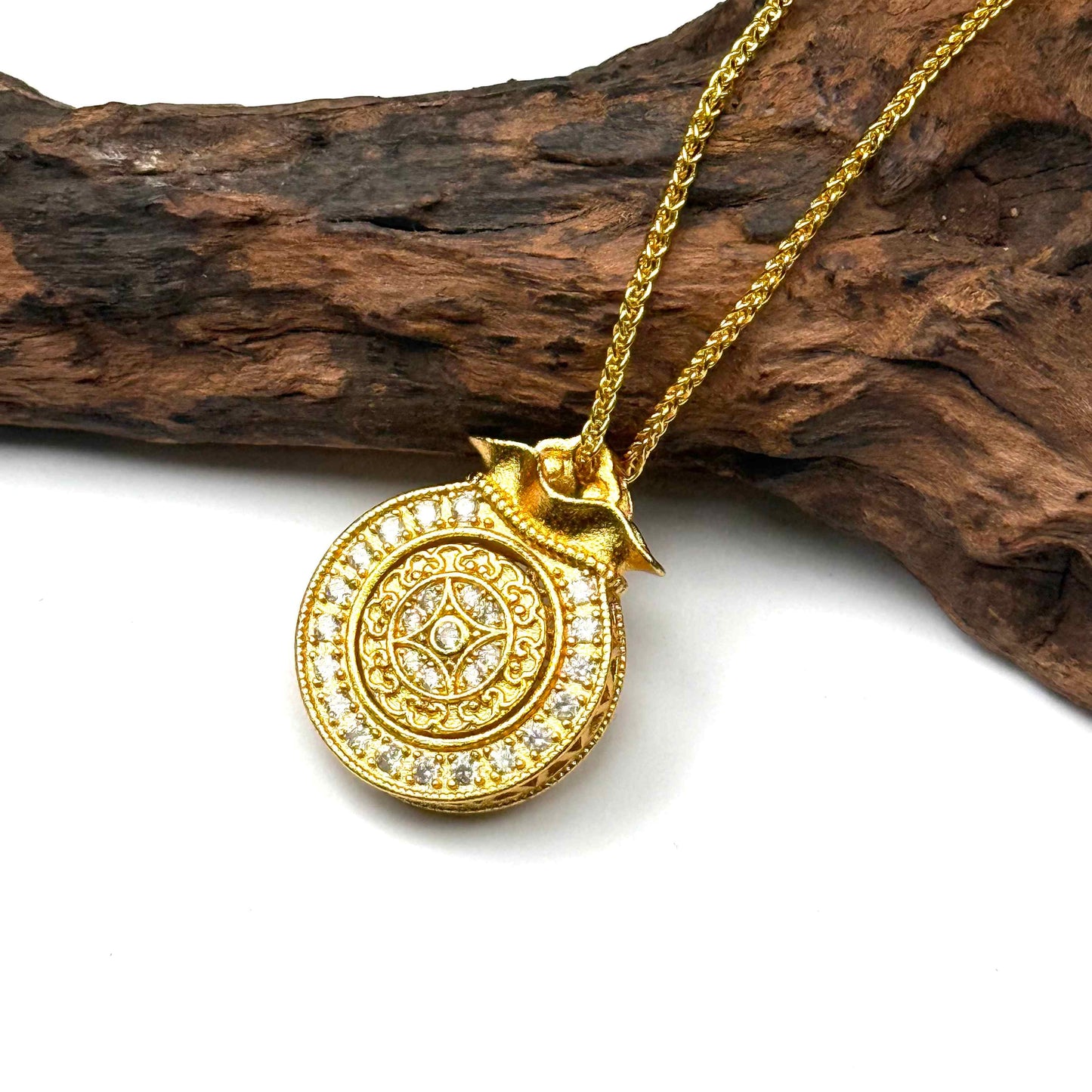 The embossed all-gold sunburst filigree back side of a round sand gold money bag charm displayed elegantly on natural driftwood background.