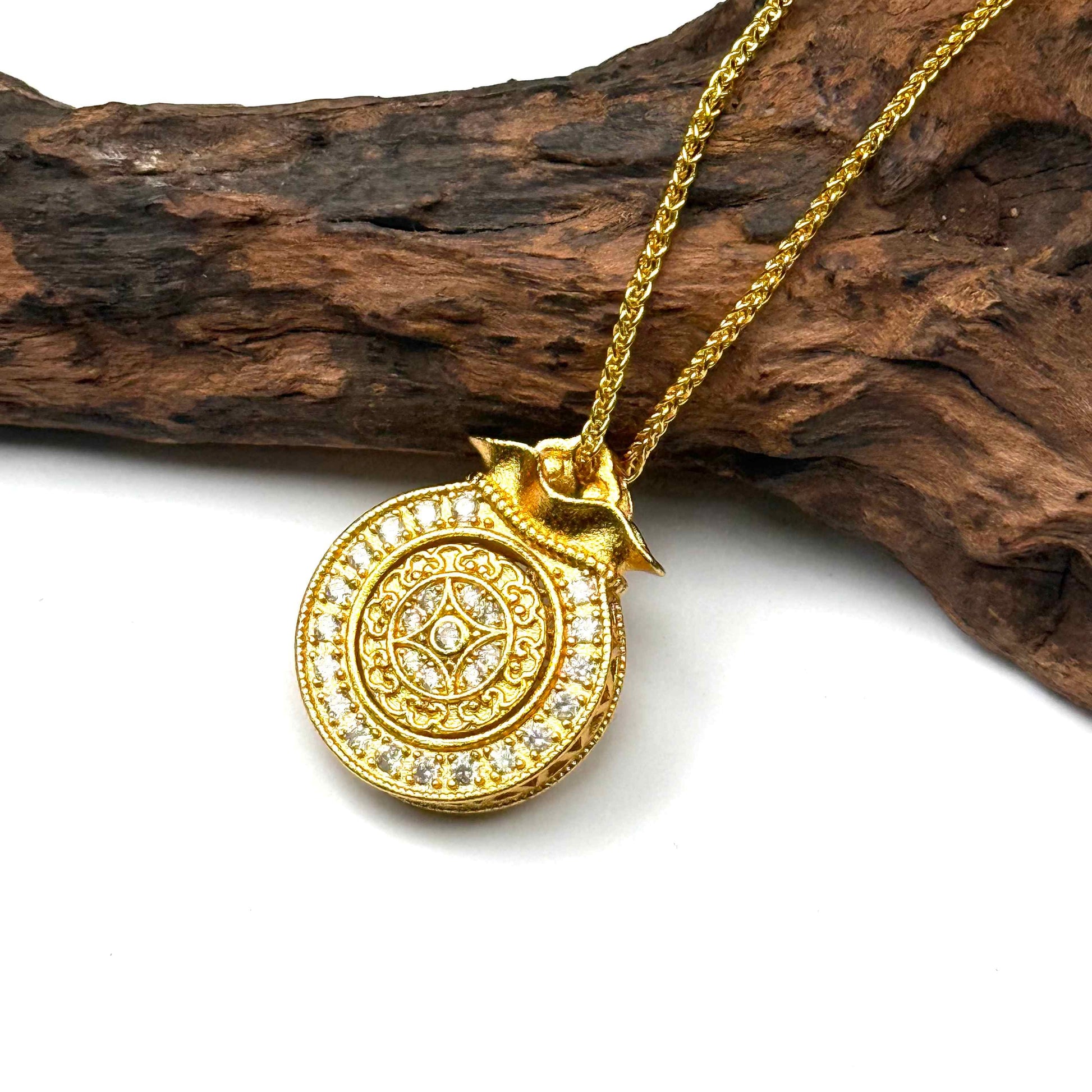 The embossed all-gold sunburst filigree back side of a round sand gold money bag charm displayed elegantly on natural driftwood background.