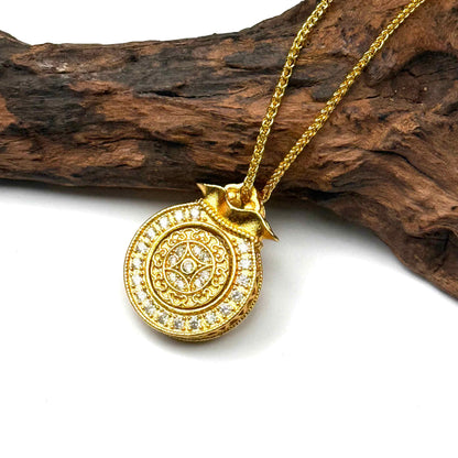 The embossed all-gold sunburst filigree back side of a round sand gold money bag charm displayed elegantly on natural driftwood background.