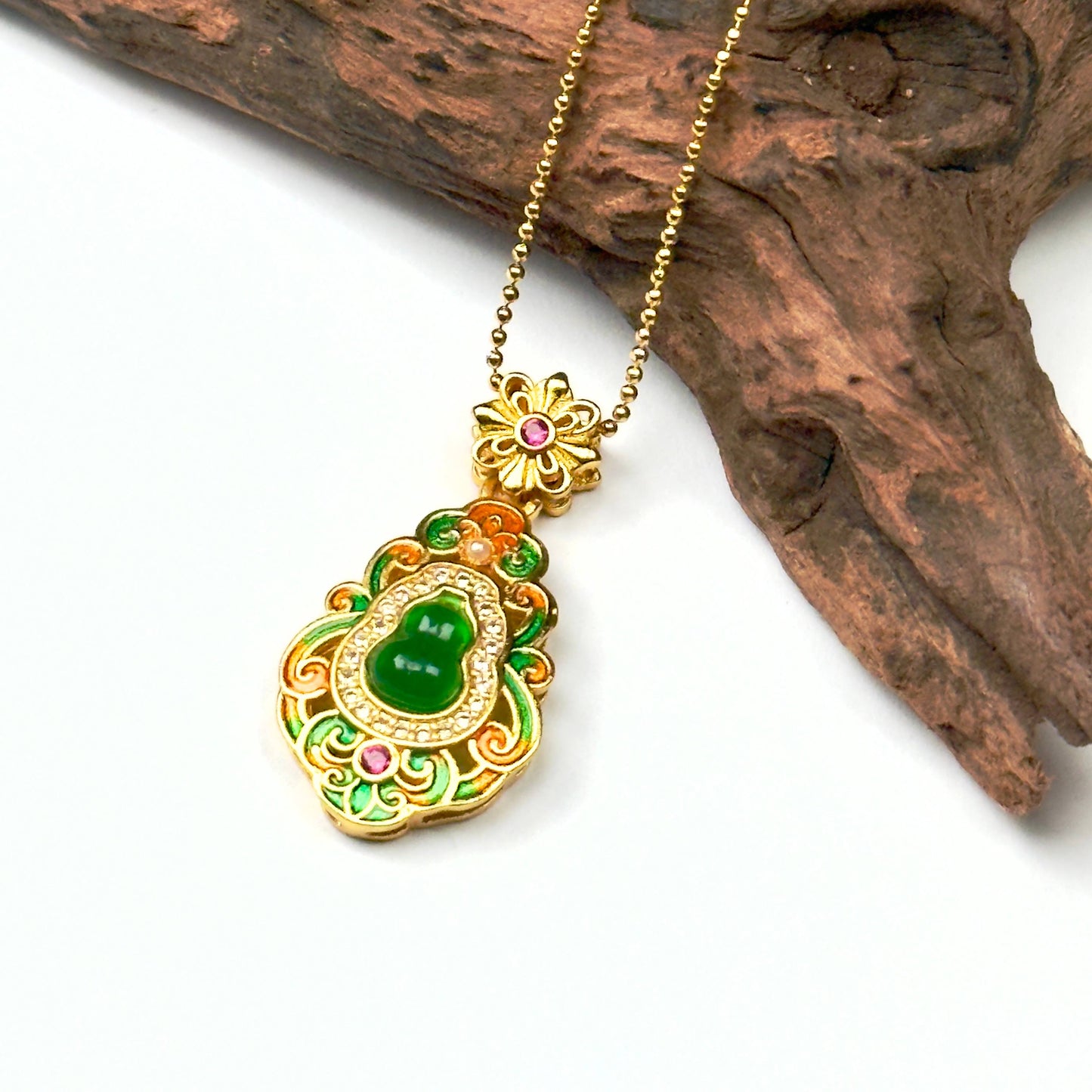 A regal sand gold enamel gourd talisman with a glowing green jade stone core and a delicate gold bead chain, displayed elegantly against a rustic driftwood branch.