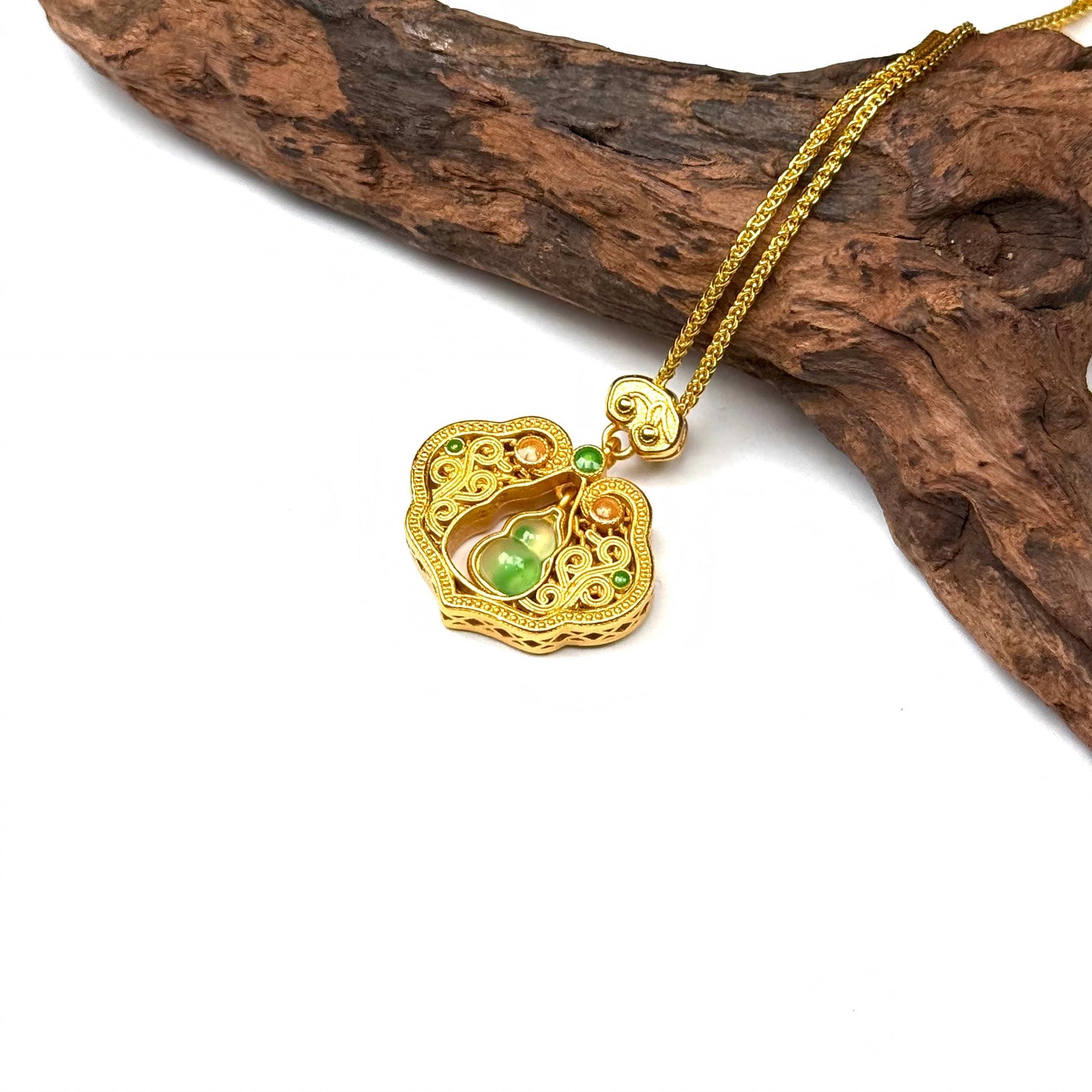 Macro top-down shot of a sand gold Ruyi lock necklace on wood, highlighting the intricate filigree and the beautiful dangling green Hulu gourd in the center.