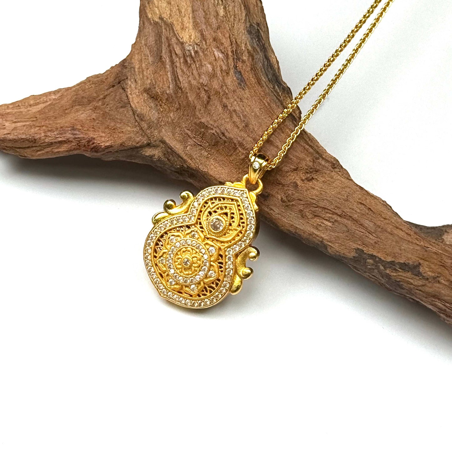 A regal sand gold Ruyi Hulu locket style amulet pendant adorned with shimmering pavé crystal rhinestones and connected to a premium gold rope chain, displayed elegantly against rustic wood.