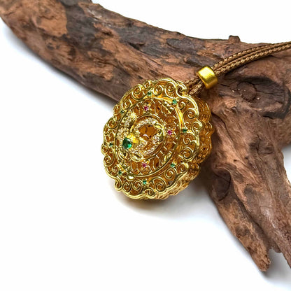 A luxurious circular sand gold Gau box amulet pendant decorated with gemstones, resting elegantly against natural rustic wood.