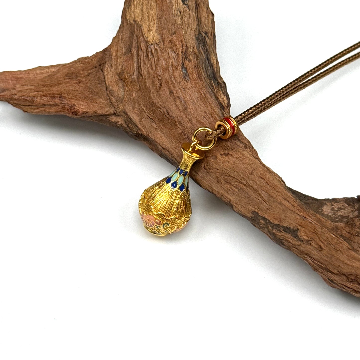 A traditional sand gold peace vase amulet resting elegantly on a piece of rustic driftwood, highlighting its Zen aesthetic, golden luster, and colorful enamel patterns.